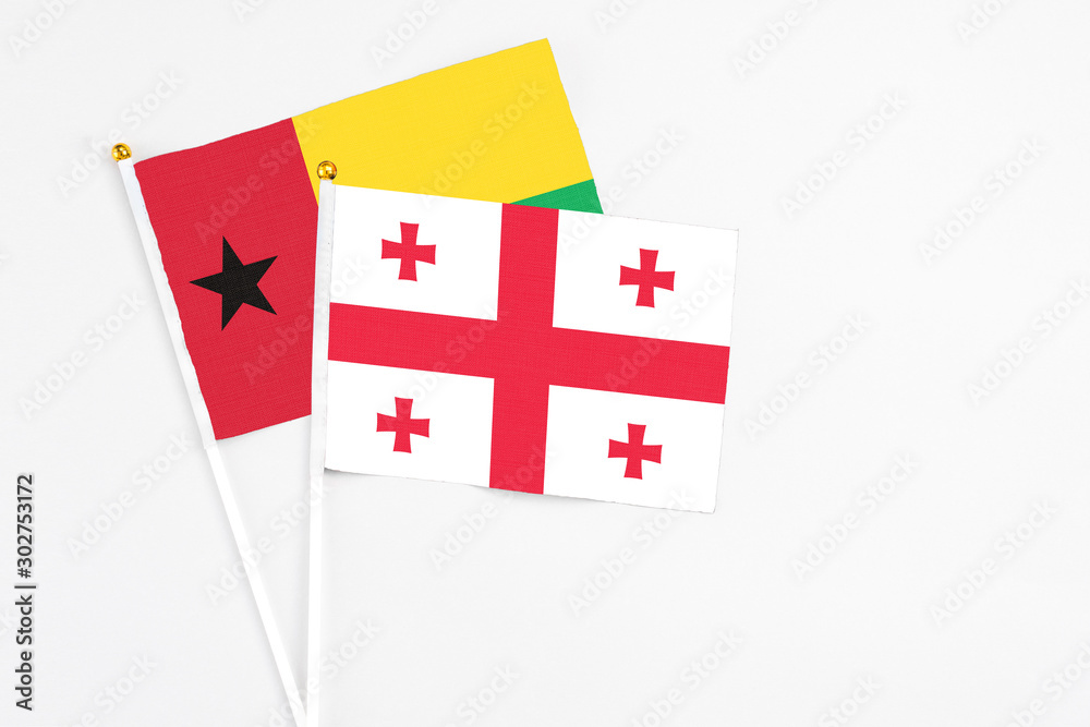 Georgia and Guinea Bissau stick flags on white background. High quality fabric, miniature national flag. Peaceful global concept.White floor for copy space.