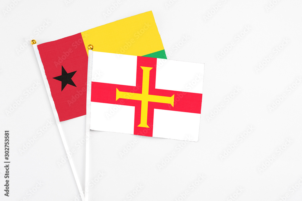 Guernsey and Guinea Bissau stick flags on white background. High quality fabric, miniature national flag. Peaceful global concept.White floor for copy space.
