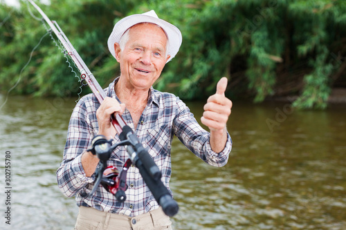 Mature fisherman with rod at riverside