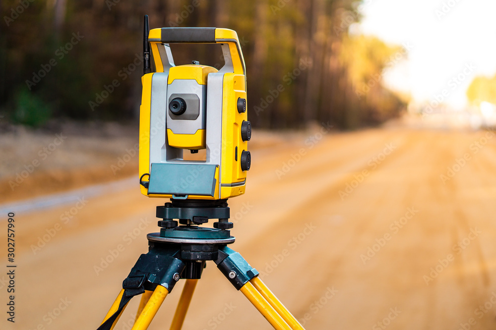 Surveyors equipment (theodolite or total positioning station) on the construction site of the road or building with construction machinery background