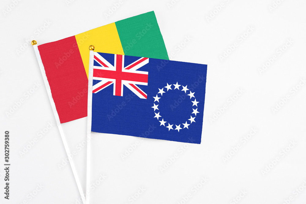 Fototapeta premium Cook Islands and Guinea stick flags on white background. High quality fabric, miniature national flag. Peaceful global concept.White floor for copy space.