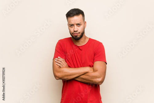 Young south-asian man frowning face in displeasure, keeps arms folded.