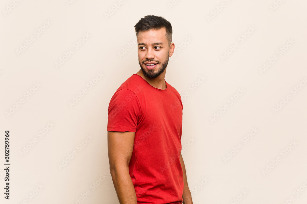 Young south-asian man looks aside smiling, cheerful and pleasant.
