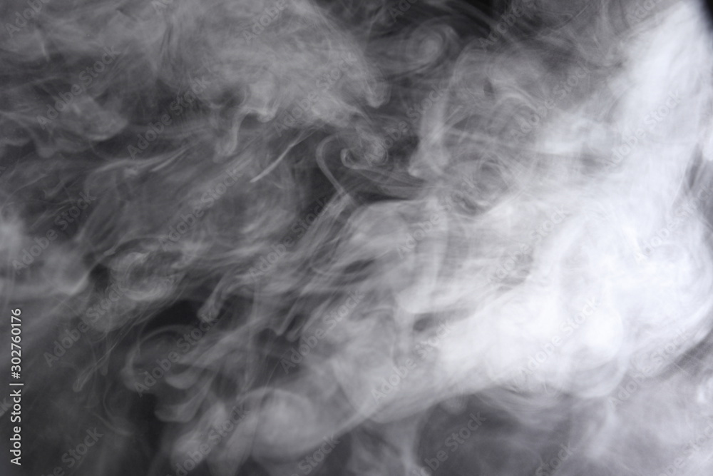 Obraz premium Puffs of white, gray smoke spread on a black background, curling in a fancy dance.