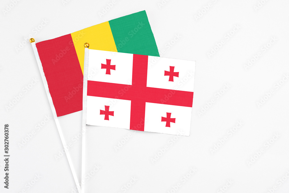 Georgia and Guinea stick flags on white background. High quality fabric, miniature national flag. Peaceful global concept.White floor for copy space.