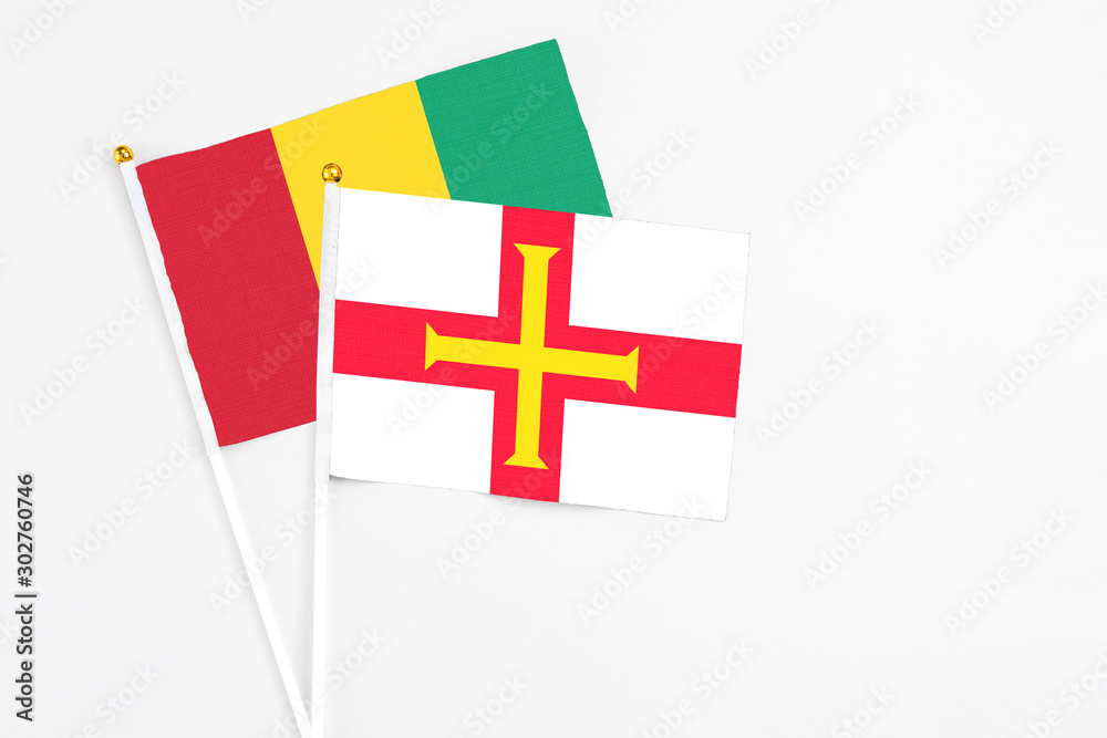 Guernsey and Guinea stick flags on white background. High quality fabric, miniature national flag. Peaceful global concept.White floor for copy space.