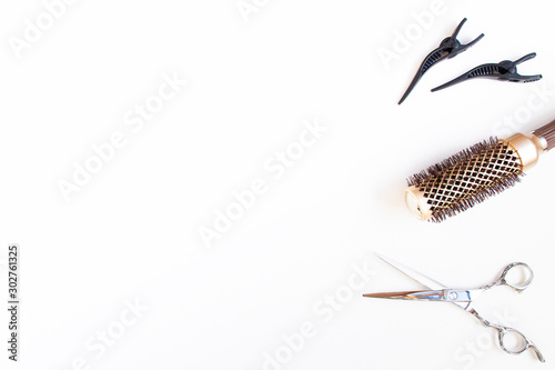 Top view flat lay of professional hair cutting shears, gold round hair brush for styling and section hair clips of the right site of the image. Hairdresser salon equipment concept, premium set.