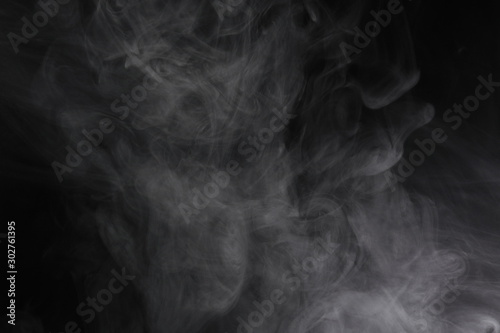 Puffs of white, gray smoke spread on a black background, curling in a fancy dance.