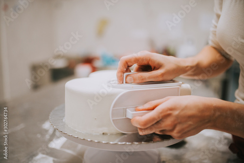 Fondant cake decoration, close-up. Skilled woman in bakery decorating cake with white fondant, copy space.