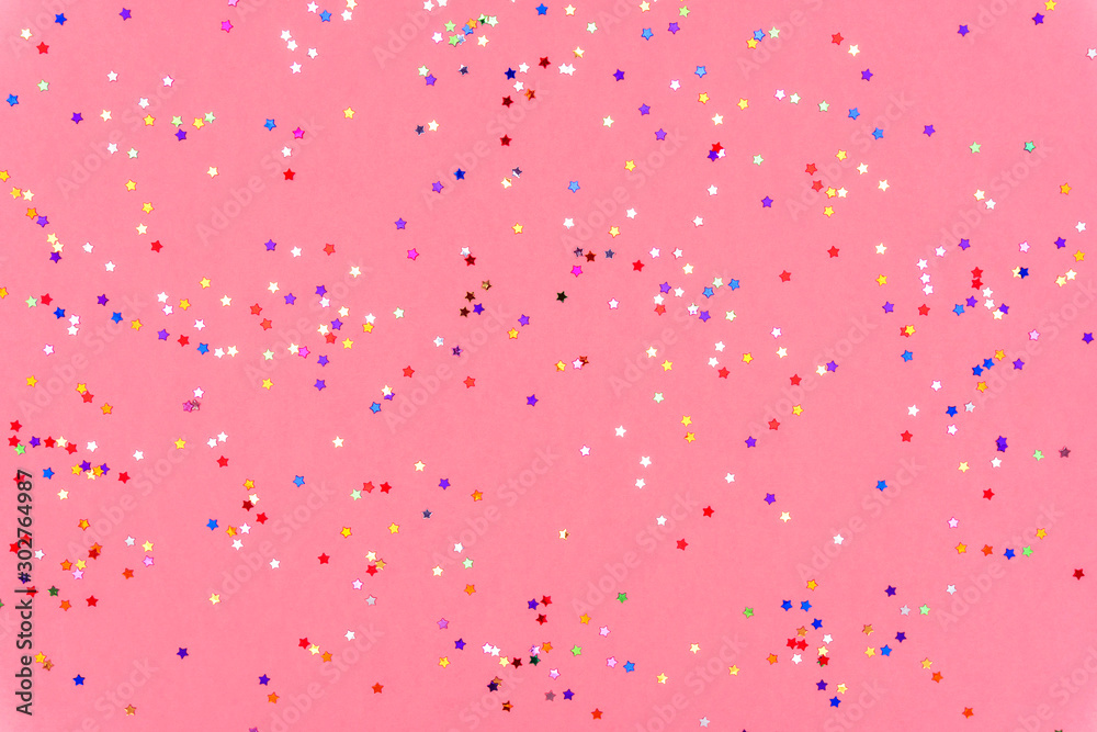 Photo of multi-colored stars glitter sprinkles on pink trendy background. Festive holiday background for your projects. Celebration concept. Christmas pattern. Top view, flat lay