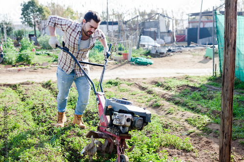 Man  professional gardener using   plow at  land with green grass in garden