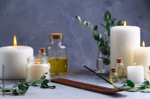 Incense stick with smoke on stone with white candles and essential oils