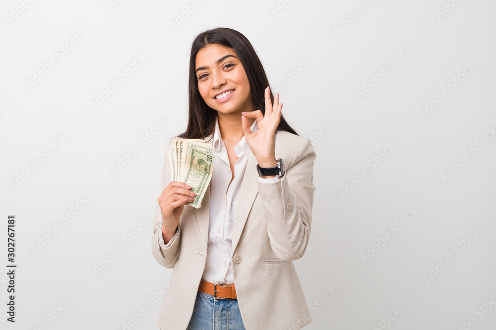 Young arab business woman holding dollars cheerful and confident showing ok gesture. Young arab business woman holding dollars cheerful and confident showing ok gesture.