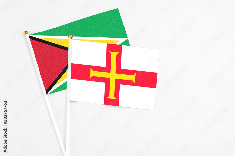 Guernsey and Guyana stick flags on white background. High quality fabric, miniature national flag. Peaceful global concept.White floor for copy space.