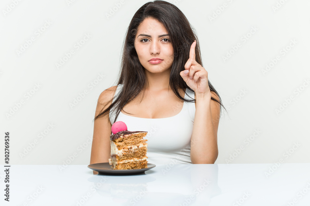 Young hispanic woman eating a cake showing number one with finger. Young hispanic woman eating a cake showing number one with finger.