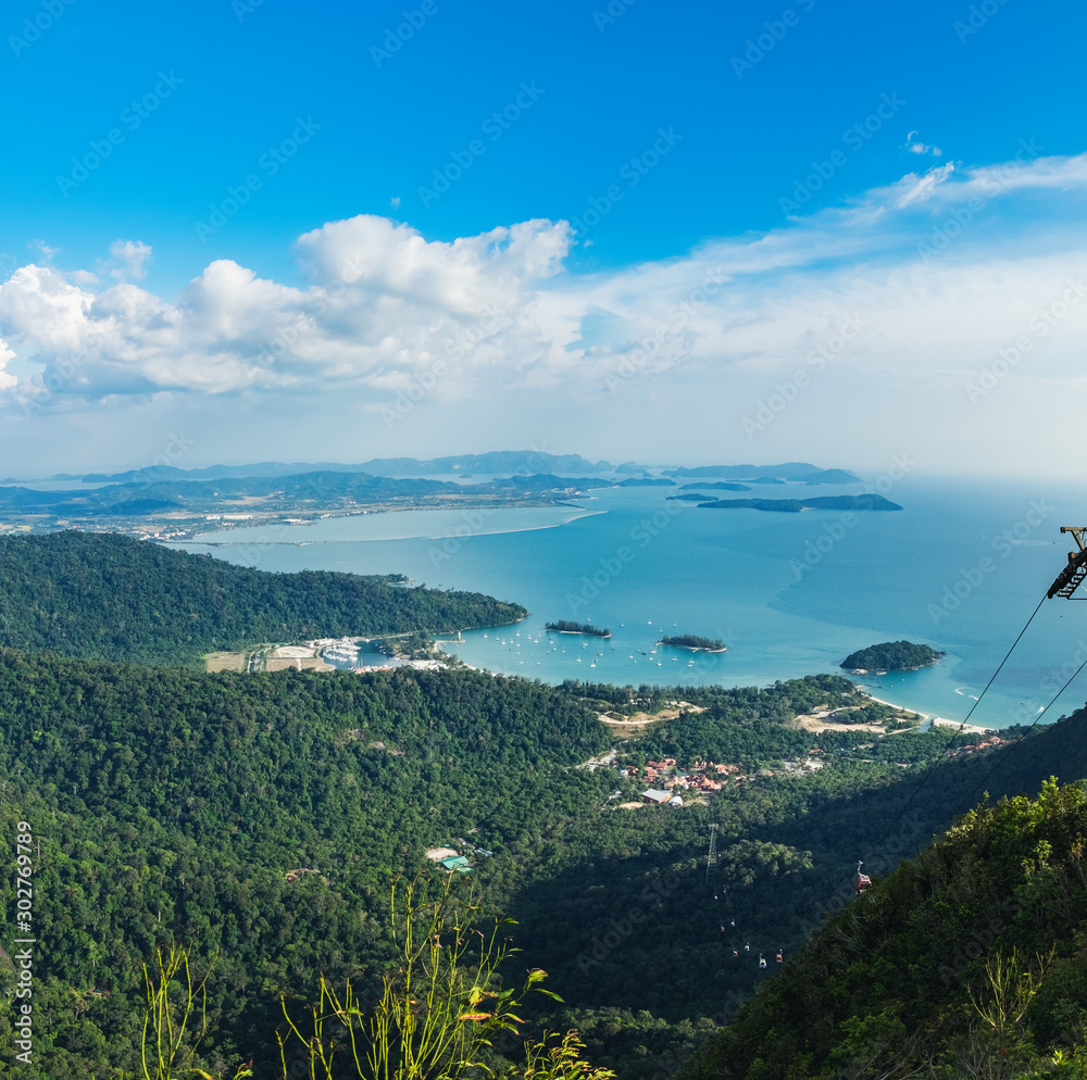 Cable Car to the top of Langkawi island and view of blue sky, sea and mountain, Malaysia, tropical plants in the foreground. Langkawi SkyCab is one of the major attractions in the island