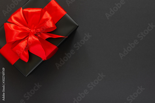 Festive background with gift, black gift box with red ribbon and bow on black background, black friday concept, flat lay, top view