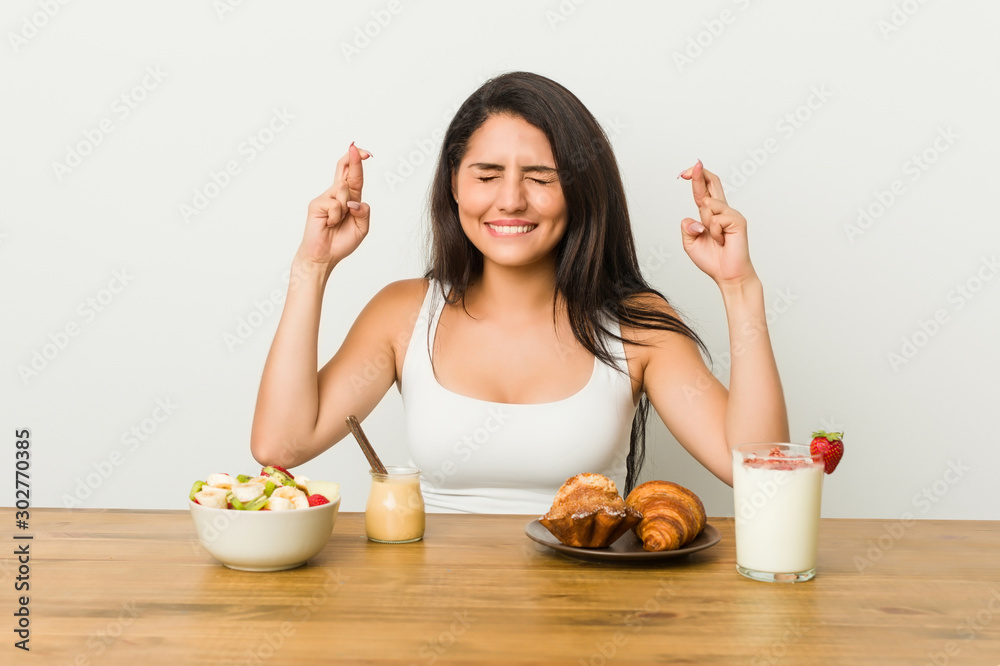Young curvy woman taking a breakfast crossing fingers for having luck Young curvy woman taking a breakfast crossing fingers for having luck