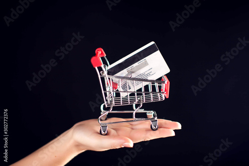 Shopping trolley model with credi card inside on woman's hand with black background. Purchases and shopping concept photo