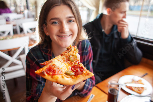 young girl eating a slice of pizza indoors, girl student gives pizza, close-up