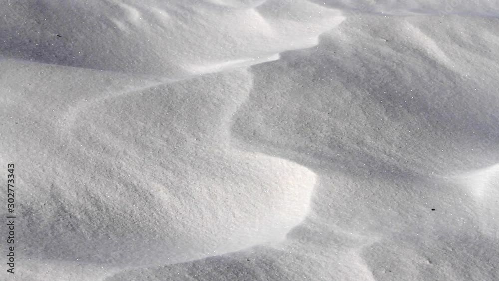 White sand being blown over the tiny ridges of a large desert sand dune.