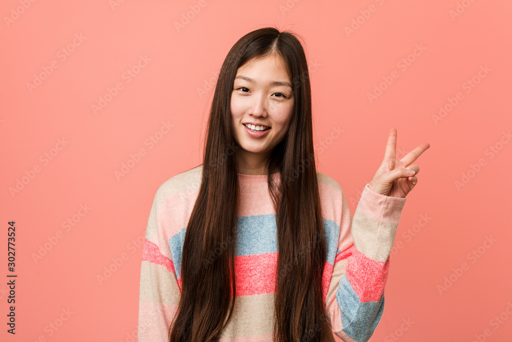 Young cool chinese woman joyful and carefree showing a peace symbol with fingers. Young cool chinese woman joyful and carefree showing a peace symbol with fingers.