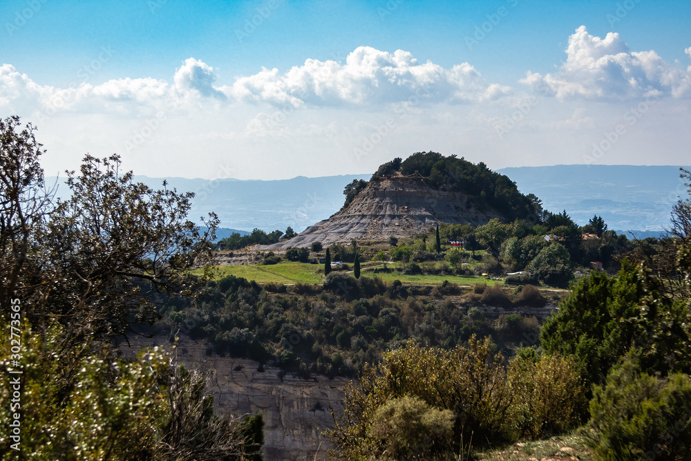 A hill surrounded with forest and small village with blue sky and clouds as the background. Tavertet, Barcelona province, Catalonia.