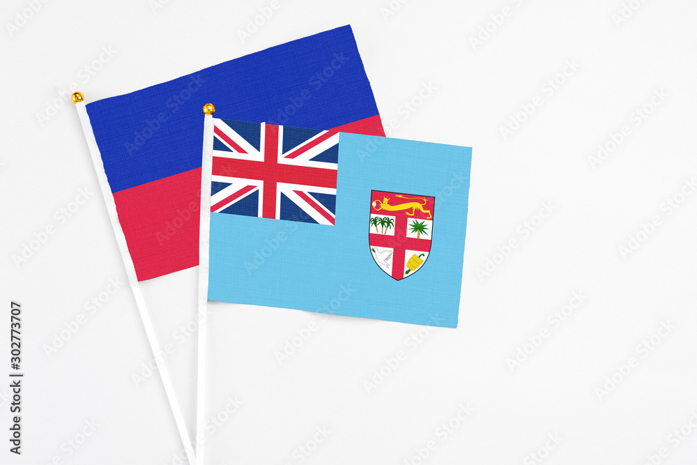 Fototapeta premium Fiji and Haiti stick flags on white background. High quality fabric, miniature national flag. Peaceful global concept.White floor for copy space.