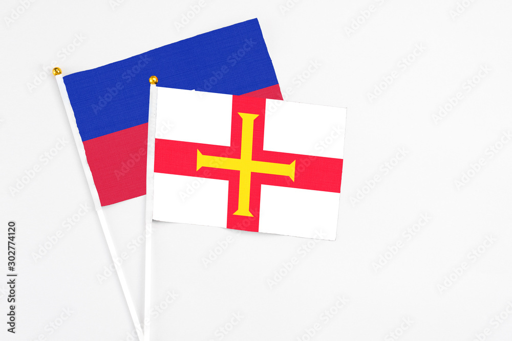 Guernsey and Haiti stick flags on white background. High quality fabric, miniature national flag. Peaceful global concept.White floor for copy space.