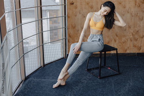 Young attractive fitness girl sitting on chair near the window on the background of a wooden wall, resting on yoga classes