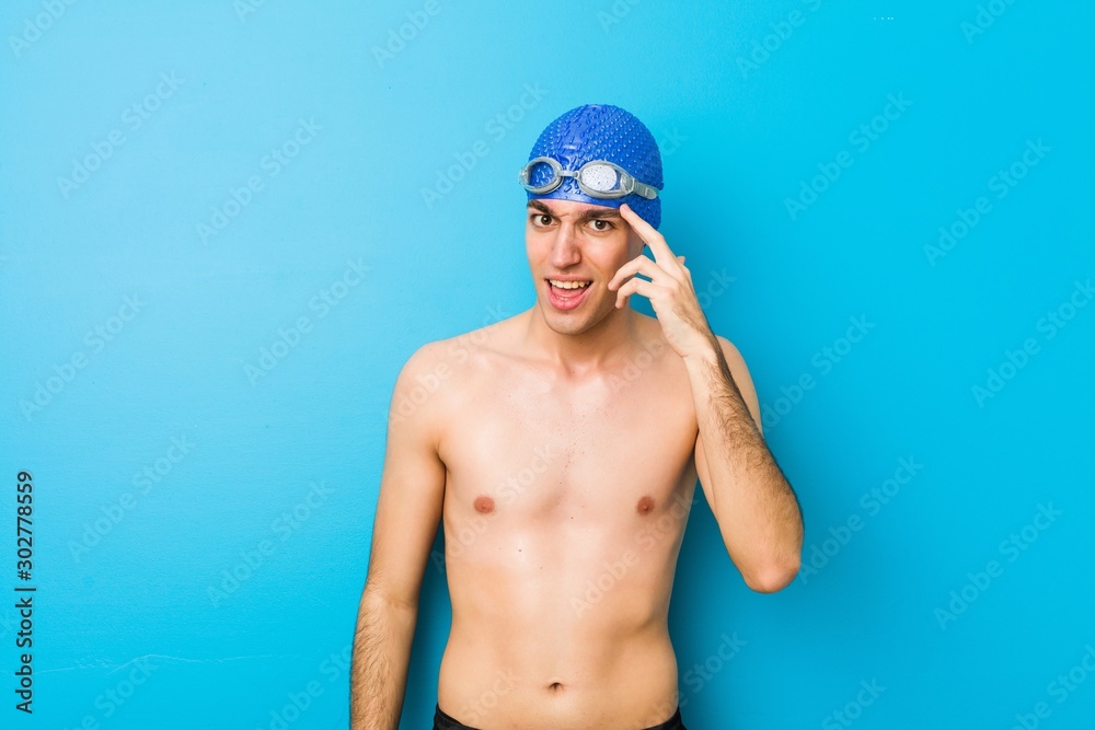 Young swimmer man showing a disappointment gesture with forefinger.