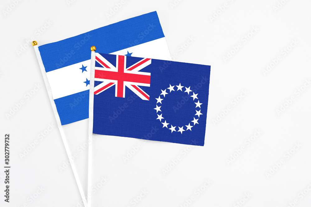 Fototapeta premium Cook Islands and Honduras stick flags on white background. High quality fabric, miniature national flag. Peaceful global concept.White floor for copy space.
