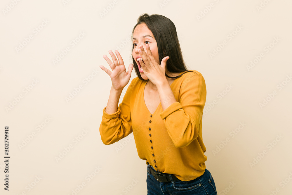 Young hispanic woman against a beige background shouts loud, keeps eyes opened and hands tense. Young hispanic woman against a beige background shouts loud, keeps eyes opened and hands tense.