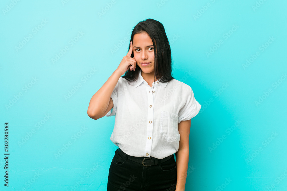 Young hispanic cool woman against a blue wall pointing temple with finger, thinking, focused on a task. Young hispanic cool woman against a blue wall pointing temple with finger, thinking, focused on a task.