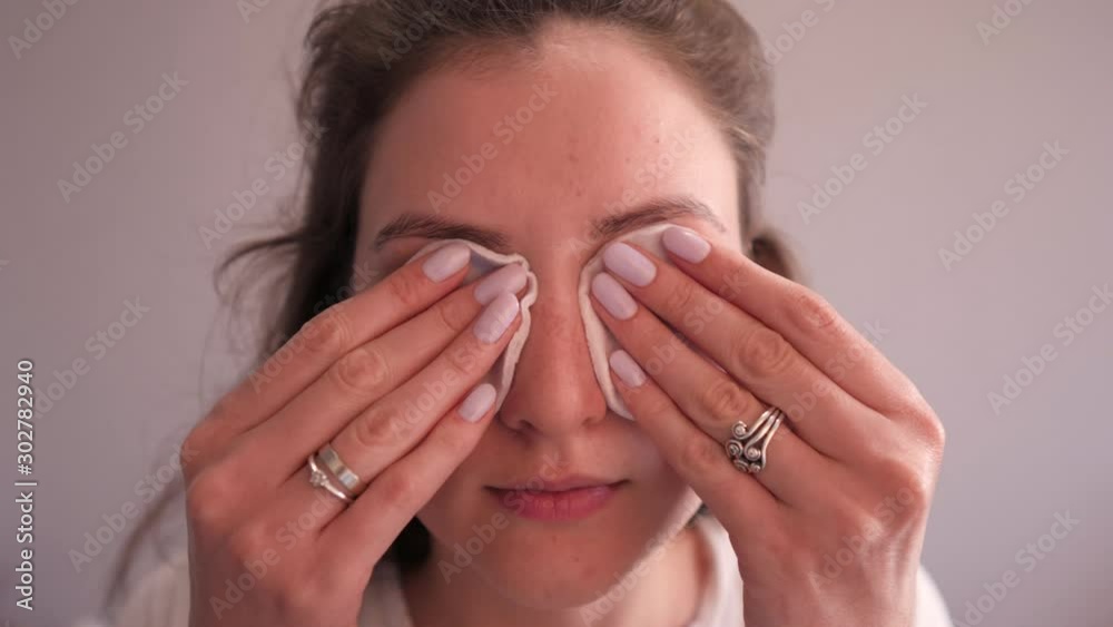 Cute young woman with clean face skin removes makeup from eyes with cotton pads. Makeup remover. Cosmetic skin care Cute young woman with clean face skin removes makeup from eyes with cotton pads. Makeup remover. Cosmetic skin care
