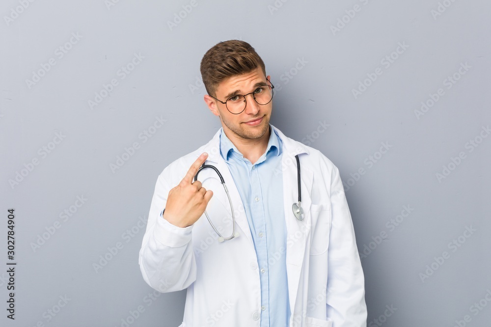 Young blonde doctor man pointing with finger at you as if inviting come closer. Young blonde doctor man pointing with finger at you as if inviting come closer.