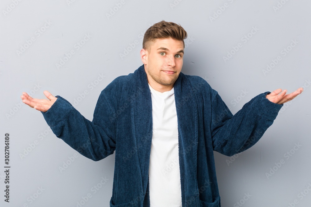Young caucasian man wearing pajama doubting and shrugging shoulders in questioning gesture. Young caucasian man wearing pajama doubting and shrugging shoulders in questioning gesture.