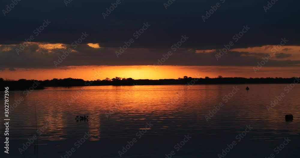 Colorful sunset at a river. Movement of water current with reflections of orange and black colours of the sky over water surface. Sun and silhouette of the coast at horizon. Soriano Colorful sunset at a river. Movement of water current with reflections of orange and black colours of the sky over water surface. Sun and silhouette of the coast at horizon. Soriano