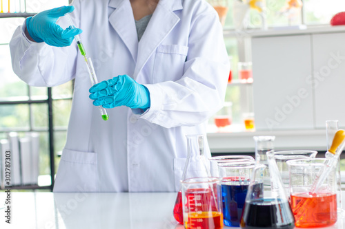 scientist wearing lab coat and gloves taking a sample in syringe while working over scientific experiment in laboratory