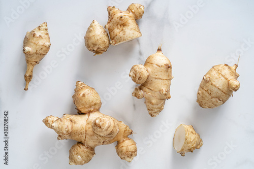 Root of topinabour on a white marble background. Jerusalem artichokes called sunroot.