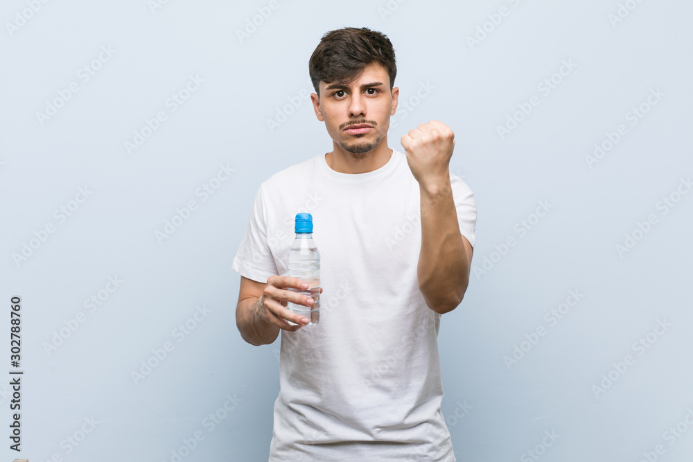 Young hispanic man holding a water bottle showing fist to camera, aggressive facial expression. Young hispanic man holding a water bottle showing fist to camera, aggressive facial expression.