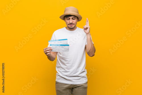 Young hispanic man holding an air tickets crossing fingers for having luck