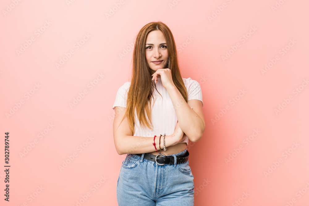 Young redhead ginger woman against a pink wall smiling happy and confident, touching chin with hand. Young redhead ginger woman against a pink wall smiling happy and confident, touching chin with hand.