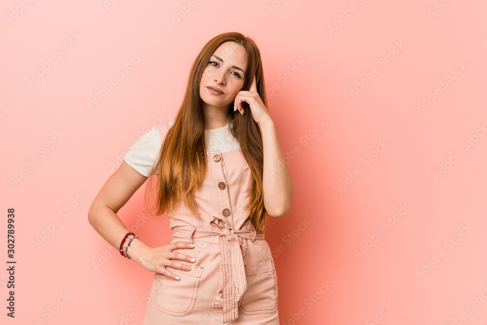 Young ginger woman with freckles pointing temple with finger, thinking, focused on a task. Young ginger woman with freckles pointing temple with finger, thinking, focused on a task.