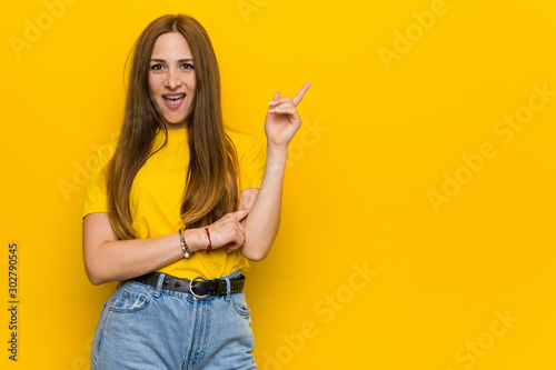 Young ginger redhead woman smiling cheerfully pointing with forefinger away.