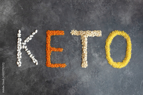 Keto word made from ketogenic food. Keto, Ketogenic diet, low carb. Healthy food concept - top view. Organic products: lentils, oatmeal, beans, millet on a dark gray background. photo