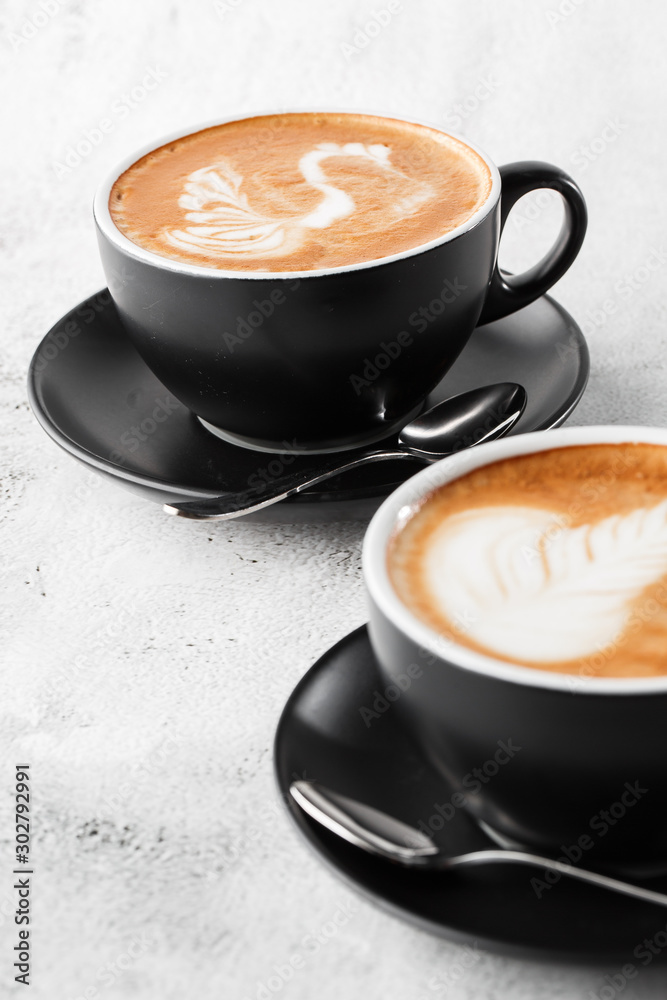 Two black cups of hot latte coffee with beautiful milk foam latte art texture isolated on bright marble background. copy space. Advertising for cafe menu. Coffee shop menu. Vertical photo.