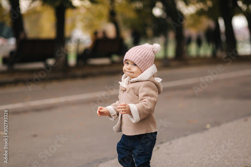 Little baby eleven month walking in the park. Happy baby in cute brown coat, pink hat and denim jeans