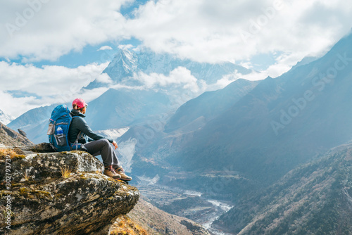 Young hiker backpacker female sitting on the cliff edge and enjoying Ama Dablam 6,812m peak view during Everest Base Camp (EBC) trekking route near Phortse, Nepal. Active vacations concept image photo