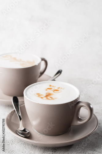 Two white cups of hot latte coffee with beautiful milk foam latte art texture isolated on bright marble background. Overhead view, copy space. Advertising for cafe menu. Vertical photo.